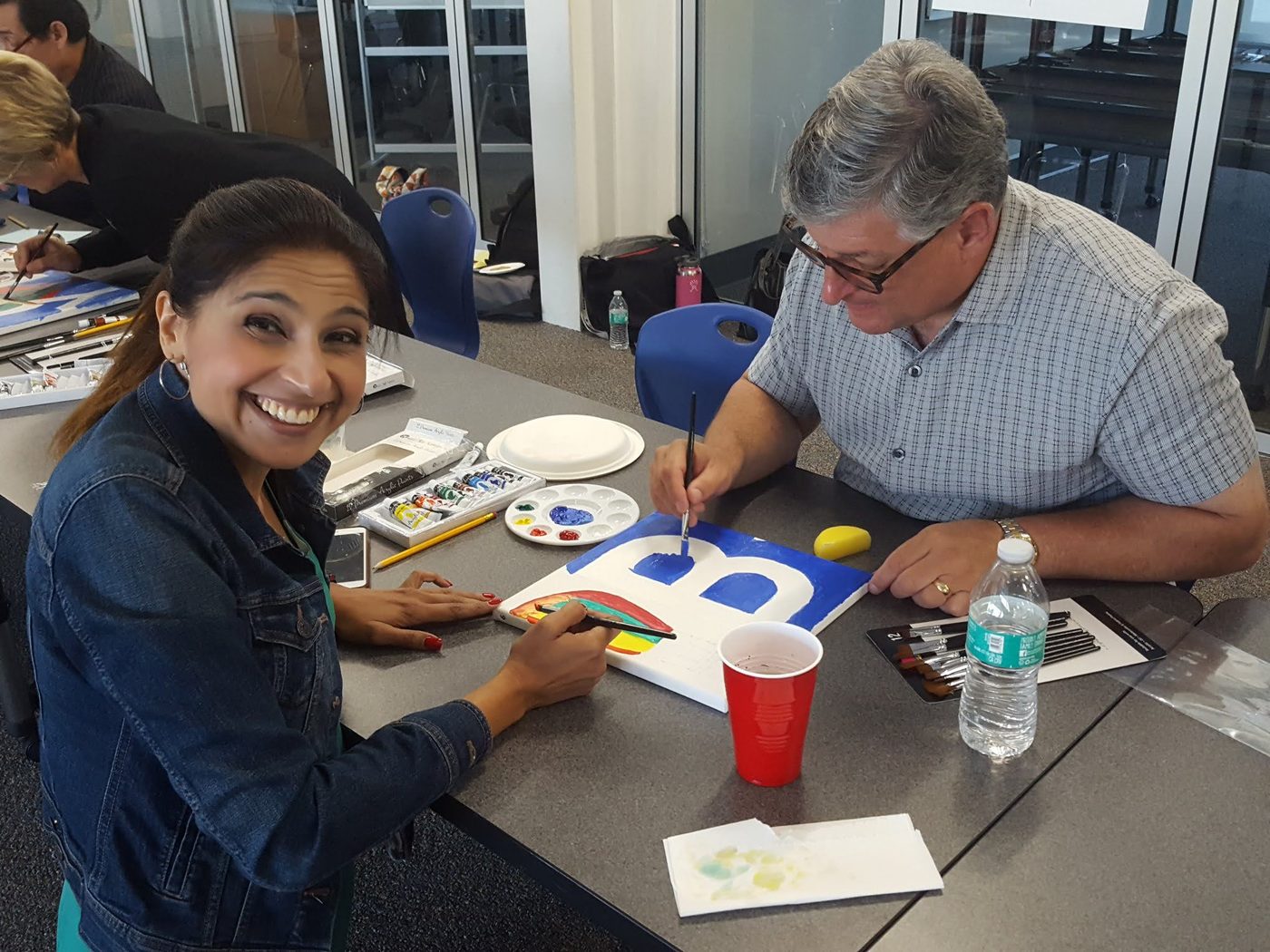 A participant smiling while painting beside her teammate